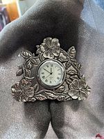 Photo of Lennox pewter clock showing front floral design and clock face with Roman numerals and date window.