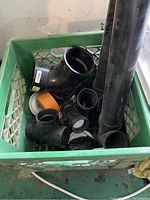 Green crate containing various ABS pipe fittings including elbows, tees, and straight pipes.