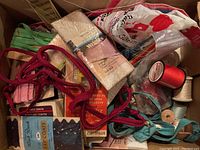 Photo showing box with assorted sewing supplies such as colored threads, lace, zippers, piping, hook and eye closures, buttons, and ribbons