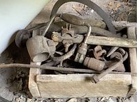 Wooden toolbox full of old logging and woodworking tools including hand brace, auger bits, axe sharpener, mallet, and other metal hand tools.