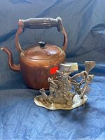 Photo showing copper kettle with wooden handle and pewter snowman figurine next to it on blue fabric background.