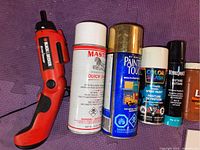 Red and black Black & Decker rechargeable screwdriver and five aerosol spray cans of various brands and purposes.