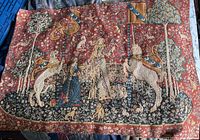 Full view of the rectangular tapestry showing the full medieval scene with unicorn, lion, two ladies, dogs, and trees against a red floral background.