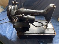 Side view of vintage black Singer Spartan sewing machine showing worn motor and electric wiring. Machine has visible dust and signs of long term storage.