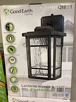 Front view of product box showing brand Good Earth Lighting and photo of black outdoor wall lantern with clear textured glass.