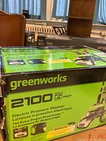 Front of boxed Greenworks pressure washer showing brand and 2100 PSI spec