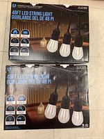 Two boxed American Lighting 48ft LED string lights placed on floor showing front of boxes with product image and branding.