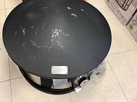 Top view of black metal round fire pit showing surface wear and Outland Firebowl branding plate.