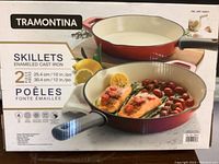 Box showing two enameled cast iron skillets by Tramontina, sizes 10 inch and 12 inch, red exterior with cream interior.