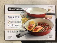 Box front showing brand Tramontina and image of the two skillets with food inside, highlighting the set contains 2 pieces sized 10 inch and 12 inch.