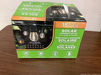 Box front showing Sunforce solar string lights with 15 LED bulbs, remote control included, LED, solar powered, and weather resistant icons visible.