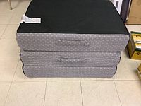 Folded mattress showing three stacked rectangular cushions with fabric handles and grey patterned fabric.