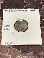 Reverse side of the 1903 British Guiana & West Indies 4 Pence silver coin showing denomination and year surrounded by a decorative wreath.