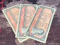 Three 1954 Canadian 2 Dollar banknotes stacked and fanned to show the front side with Queen Elizabeth II portraits.