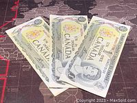 Three 1973 Canadian 1 dollar banknotes arranged overlapping on a map background