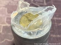 Top view showing the obverse side of the rolled 1996 twoonie coin with visible date through partially torn plastic wrapping.