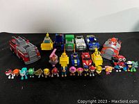 Front view of all Paw Patrol figures and vehicles arranged on table, showing variety of characters and vehicles.