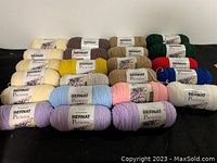 23 skeins of Bernat Premium yarn in assorted colors arranged in rows on dark surface.