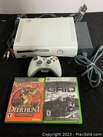 Xbox 360 console with controller, power supply, AV cable, and two games laid out on a black surface