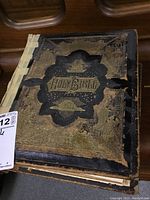 Exterior front cover of Holy Bible with black leather and gilt embossed decoration, showing wear and spine damage