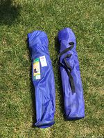 Two blue carrying bags for folding chairs placed on grass, showing overall size and condition.