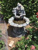 Full view of the large cement fountain bird bath outdoors among greenery. Shows water basin and upper decorative watermill.