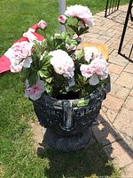 Full view of dark, heavy cement planter placed on lawn with artificial pink and white flowers inside. Shows overall size and weathered surface.