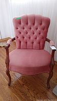 Front view of vintage armchair with pink tufted velvet upholstery and wooden frame.