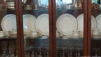 Wide view of wooden china cabinet shelf displaying Paragon Athens china set including plates and cups with silver pieces visible above