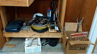 Shelf with assorted extension cords coiled, hard hats, black toolbox, and some hardware items.