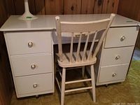 Full view of white desk with seven drawers and wooden chair in front.