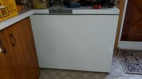 Full view of Danby white chest freezer placed in a basement corner next to cabinets and door.