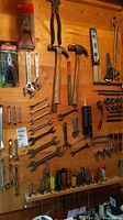 Wide view of wooden pegboard with hand tools including hammers, wrenches, socket set, screwdrivers, and level mounted for display.