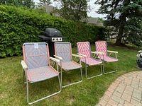 Front view of four folding lawn chairs on grass near patio and grill