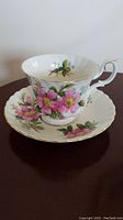 Close-up of pink floral bone china teacup and saucer with gold trim on a dark surface.