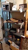 Front view of metal shelf with 5 shelves containing various household items including jars, boxes, mats, and an electric kettle on top.