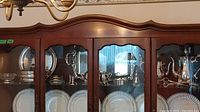 Photo of 1 shelf with silver plated trays and serving bowls inside a wooden and glass curio cabinet.