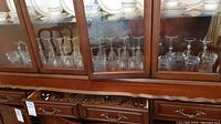 Cabinet shelf displaying multiple glass and crystal stemware including wine glasses and drink glasses.