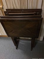 Top view of the four wooden TV tables folded and stored upright on the rack, showing wood grain rectangular tops.