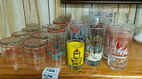 Top view of assorted vintage drinking glasses including holiday themes, Kentucky Derby, Coca-Cola, boot and 1000 Islands glasses showing variety of designs and colors.
