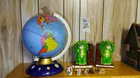 Photo of the vintage blue tin globe with colorful world map, accompanied by green frog bookends, ceramic animal figurines including flamingos