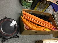 Cardboard box containing orange and black Hot Wheels track pieces and black circular Super Rally base on floor