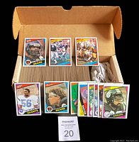 Photo showing a partial box of 1984 Topps Football cards with numerous cards stacked and some individual cards laid on top, including Bears and Steelers players