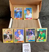Open storage box filled with 1987 OPC baseball cards; two sample cards (Mike Schmidt, Roger Clemens) standing against box lid.