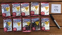 Ten unopened 1991 Soccer Shots Major Soccer League Series trading card foil packs arranged in two rows on a wooden surface alongside a permanent marker and a Maxsold lot number card.