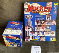 Front view of sealed wax box and empty sticker album, showing cover art and box sealed sticker pack.