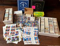 Wide view of lot contents including two large binders, several boxes filled with thousands of baseball cards, some loose cards and uncut sheets spread out, a baseball and a First Day Cover envelope.