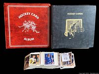 Two closed hockey card binders (one red labeled 'Hockey Card Album', one black labeled 'Hockey Cards') and multiple loose hockey cards lying in front.