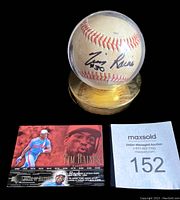 Autographed baseball in clear dome display stand with gold base, accompanied by Tim Raines baseball card and maxsold auction lot number card.