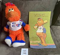 Plush Youppi doll wearing Montreal Expos jersey sitting next to a wall hanging with Youppi image and French text, all displayed on a couch.